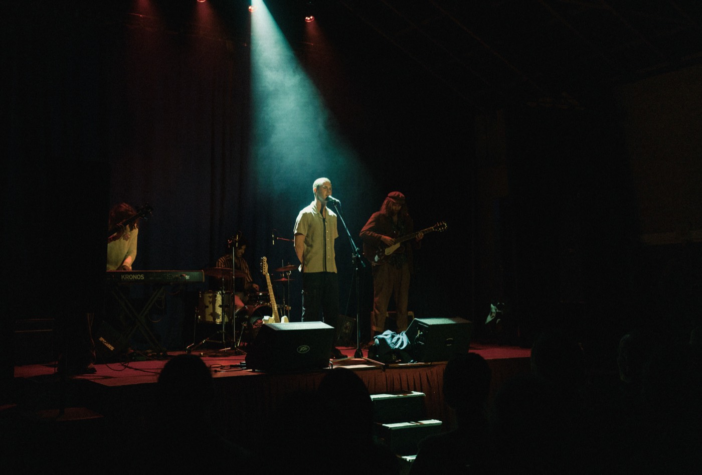 Henry West singing under a single spotlight on a dark stage, his band behind him.